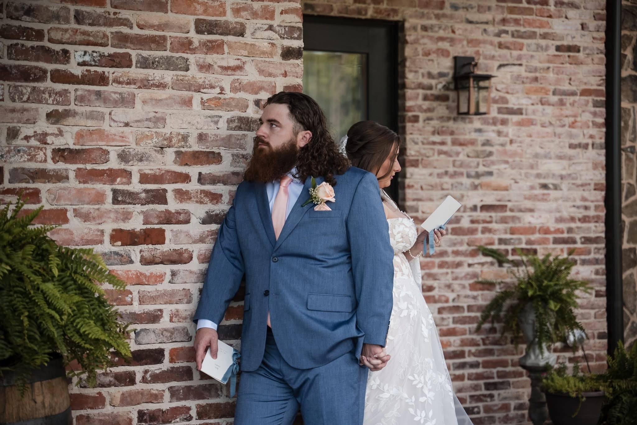 Bride and groom standing back to back against the brick wall reading their vows