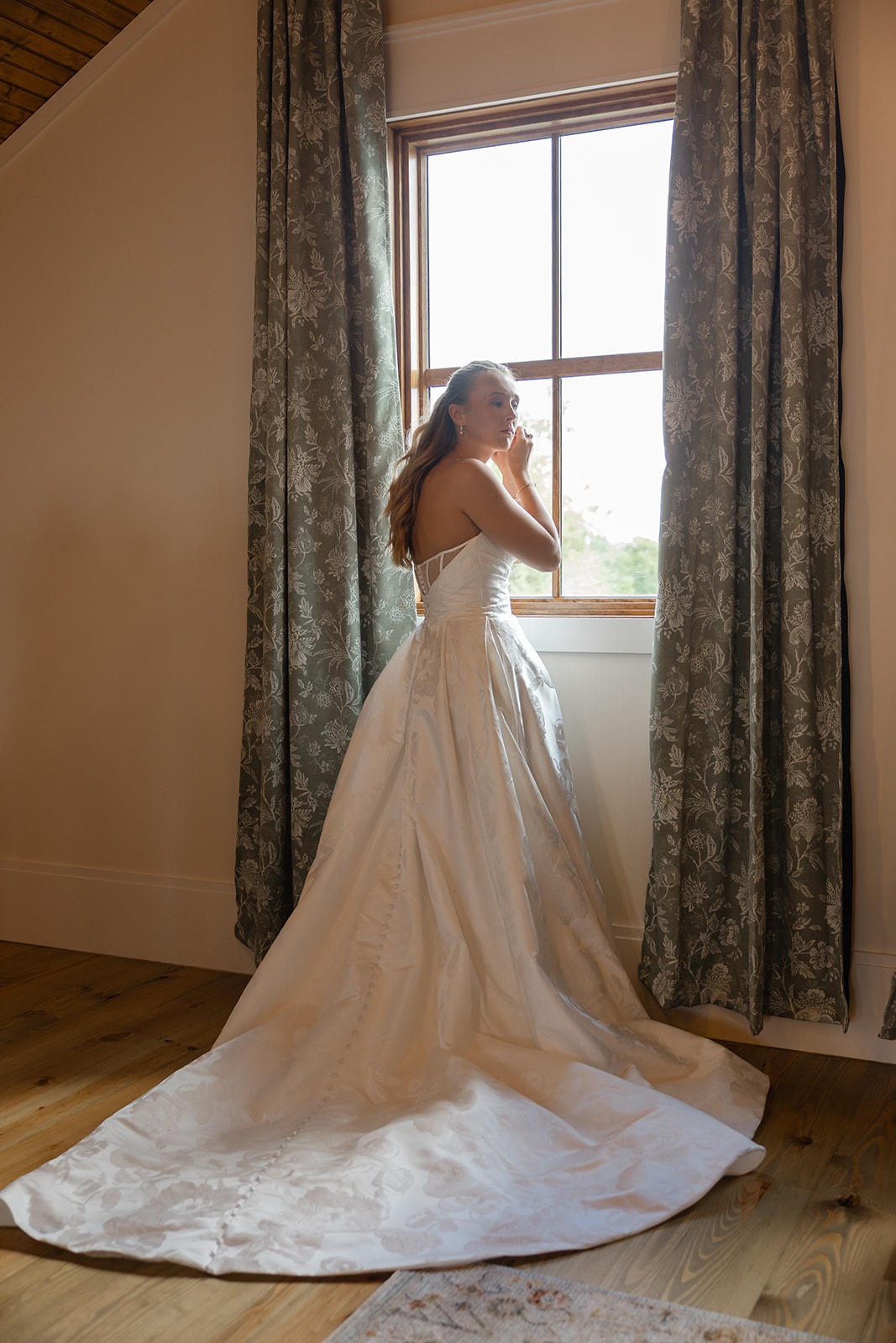 Bride in full gown with long train standing by the window in the bridal suite