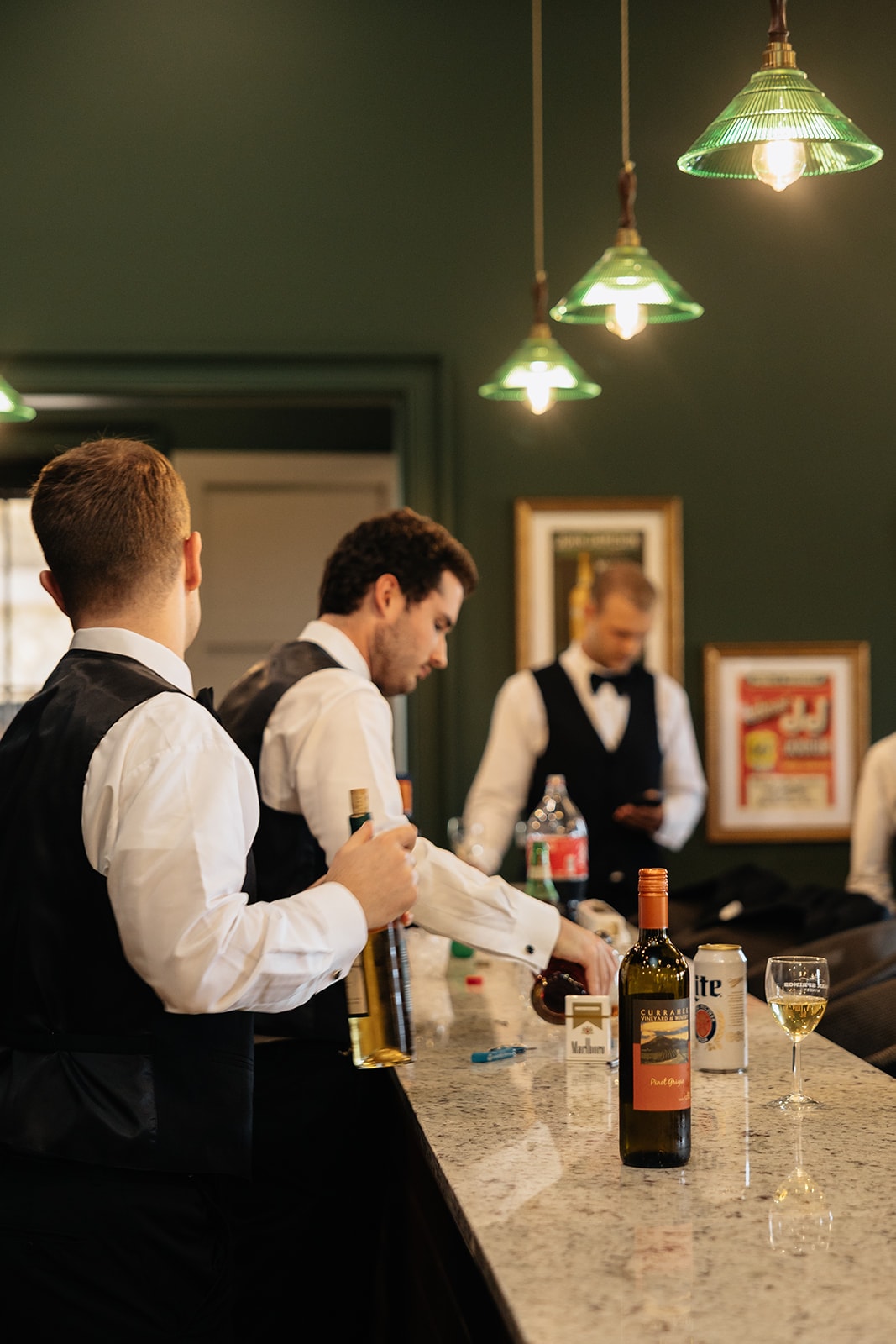Wide angle view of bartenders working behind the bar with green pendant lights