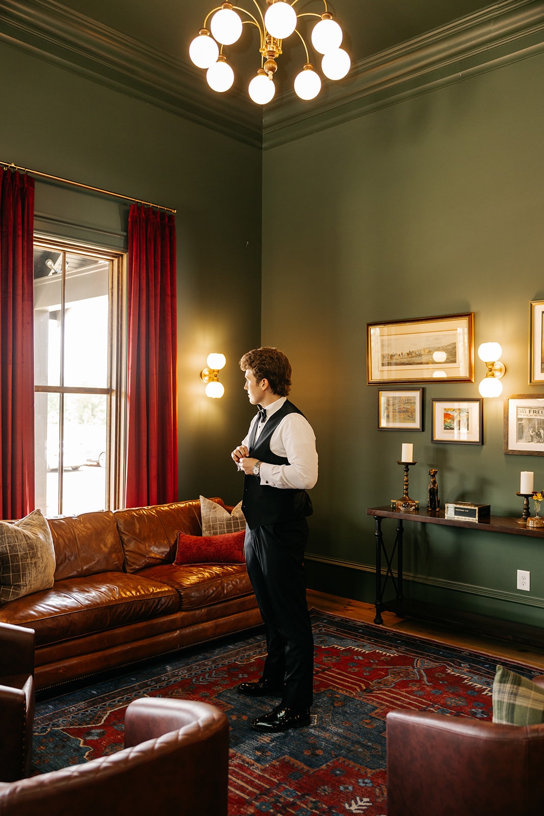 Groom standing in the tasting room with leather sofa and gold chandelier