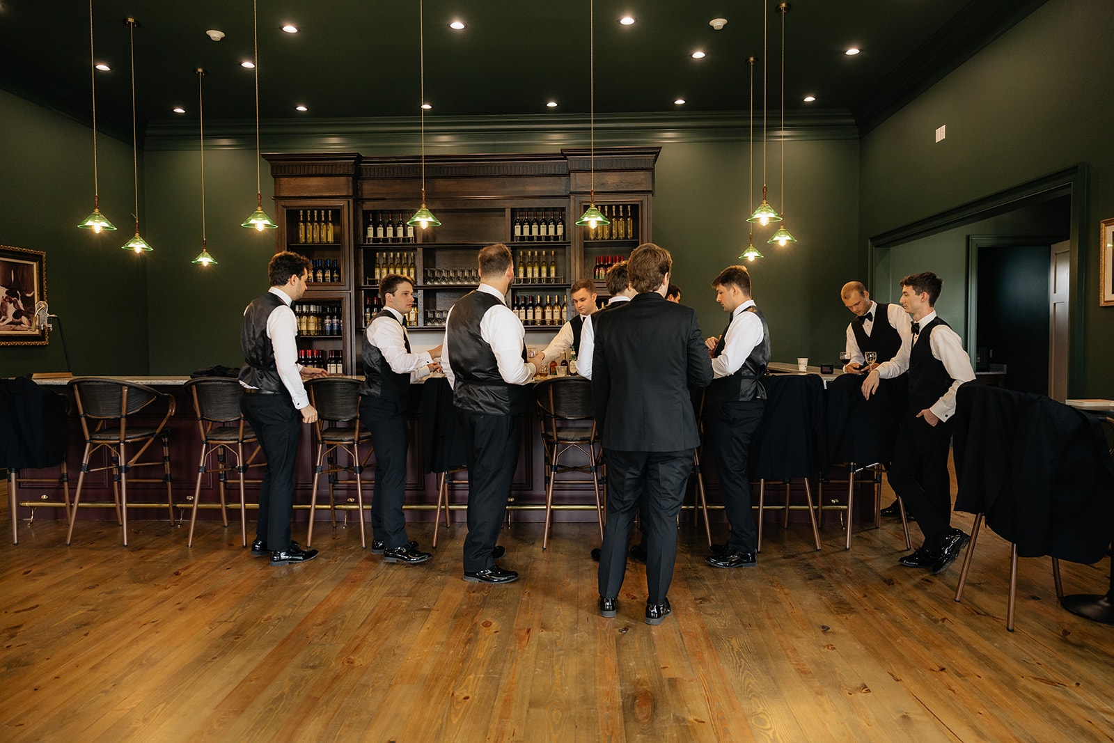 Full view of groomsmen at the bar with warm wood floors and green walls