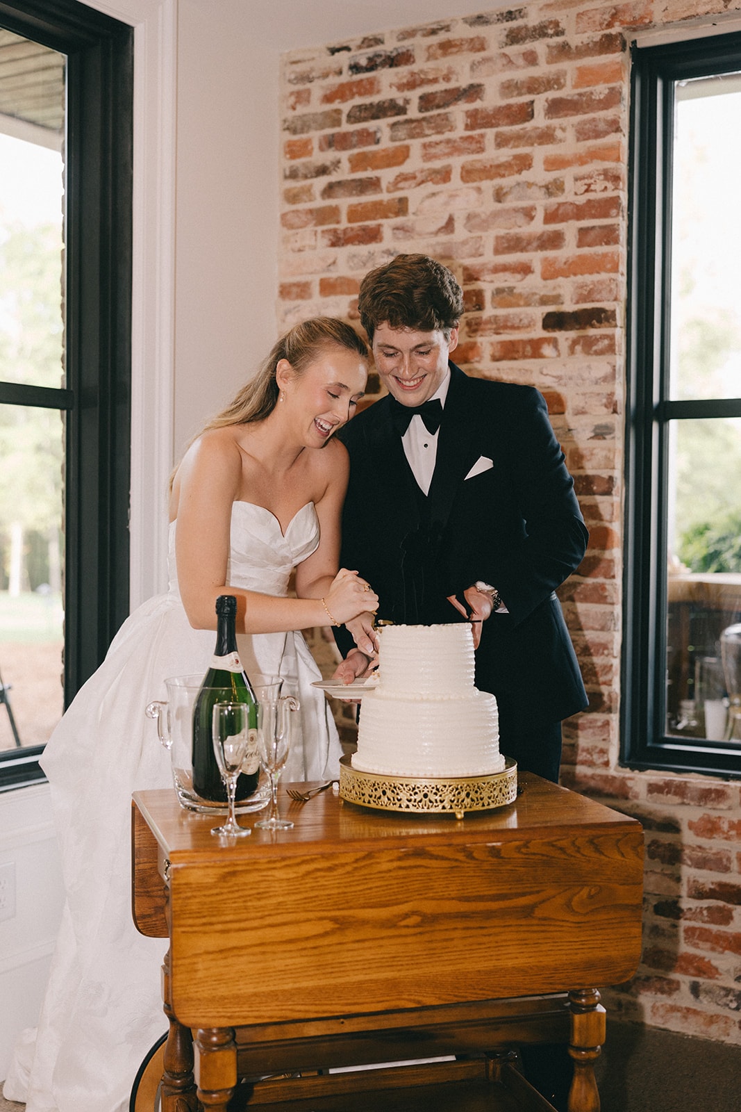 Bride and groom cutting their wedding cake by the brick wall