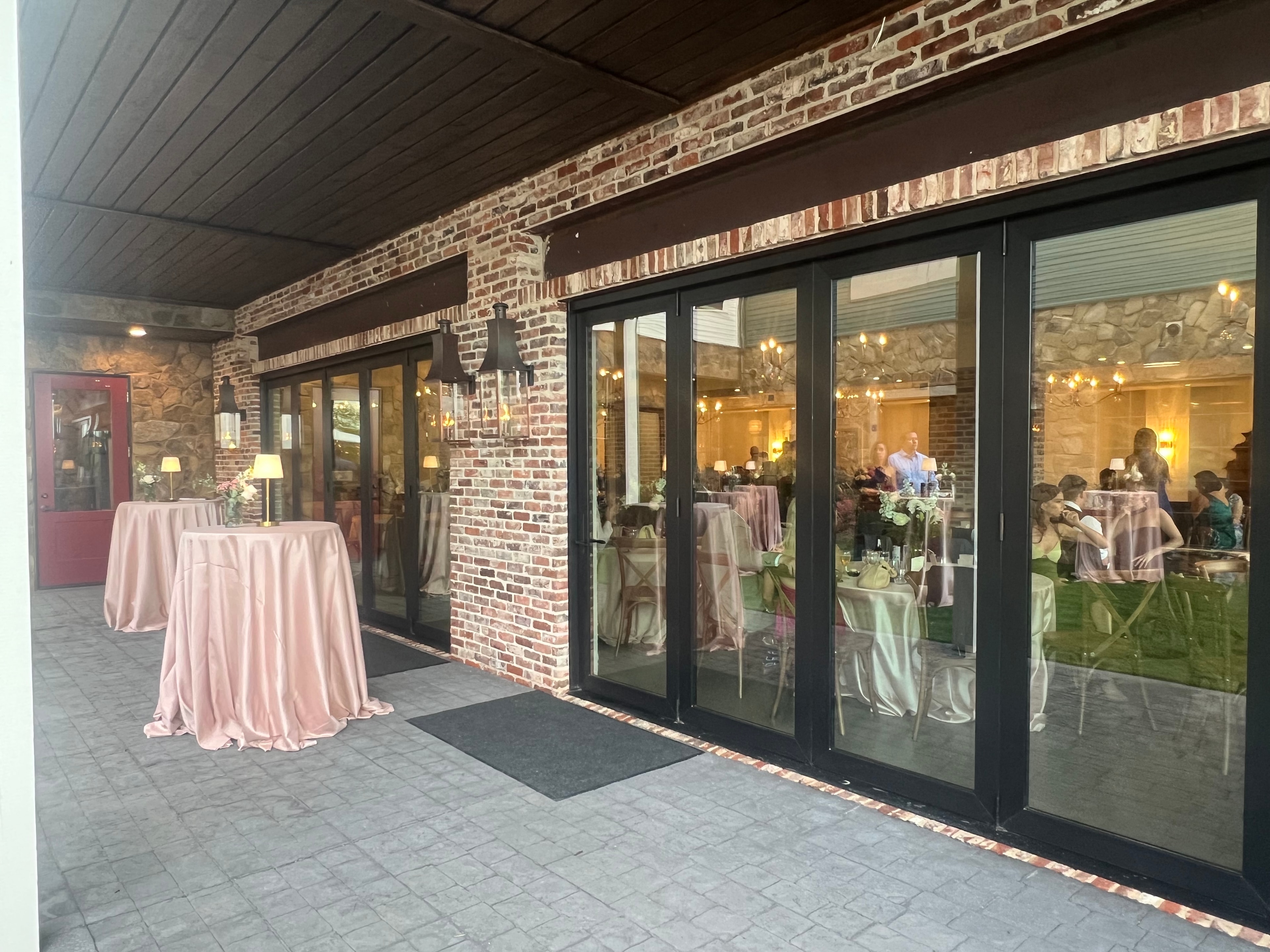 Venue exterior at evening with cocktail tables and guests visible through glass doors