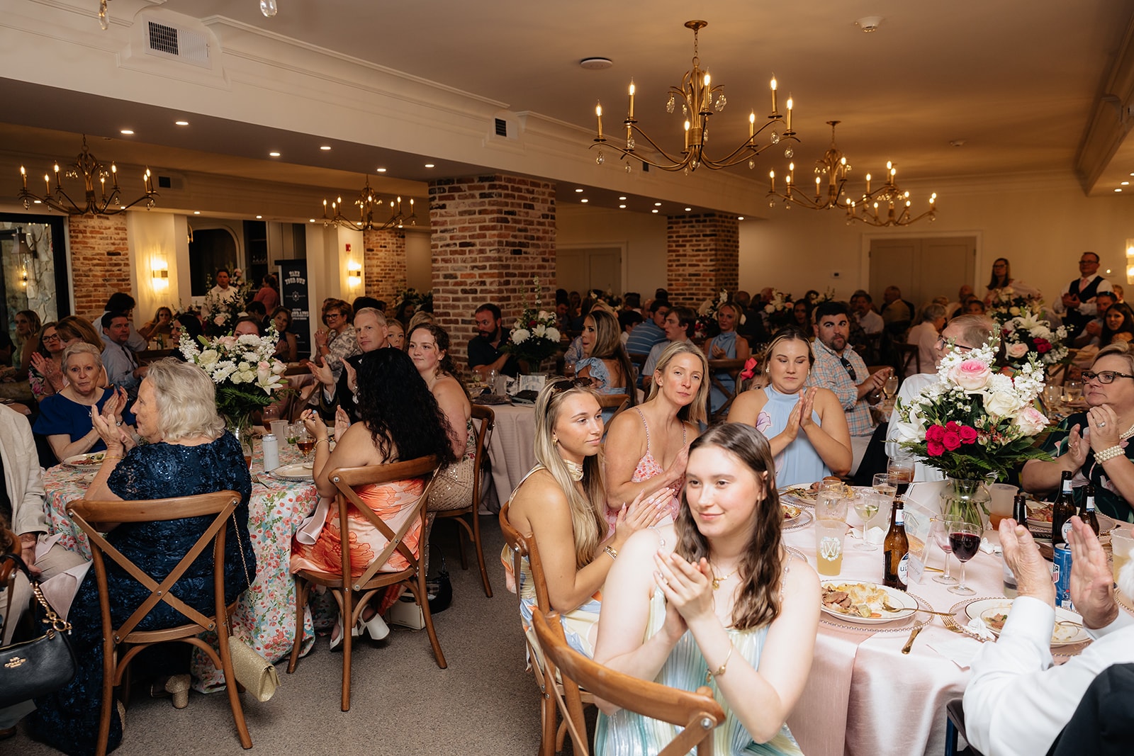 Full room of guests applauding under gold chandeliers